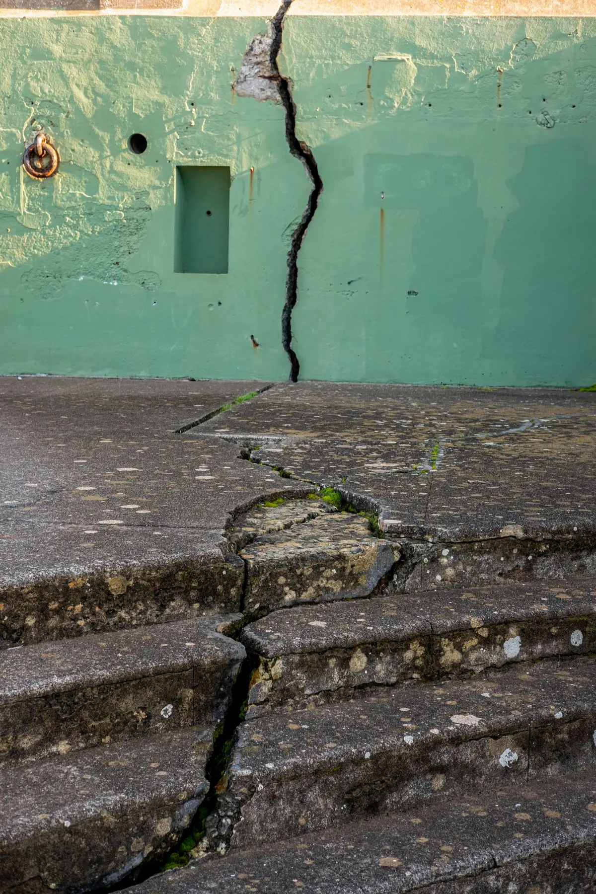 A weathered concrete wall and steps split by a wide outdoor crack.